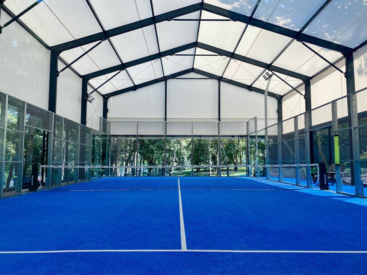 wedding-photographer-01 Spacious indoor padel court with vibrant blue flooring under a wide roof.